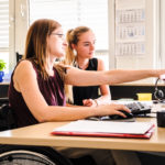 Zwei Frauen, eine im Rollstuhl, am Tisch bei einer Besprechung