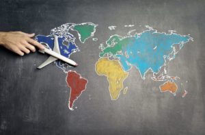 Dekorativbild: eine Hand führt ein Miniaturflugzeug über eine bunte Weltkarte