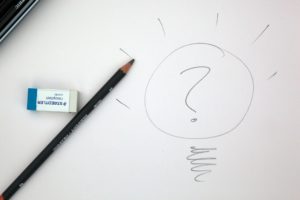 Stift und Radiergummi, daneben eine gezeichnete Glühlampe mit einem Fragezeichen in der Mitte